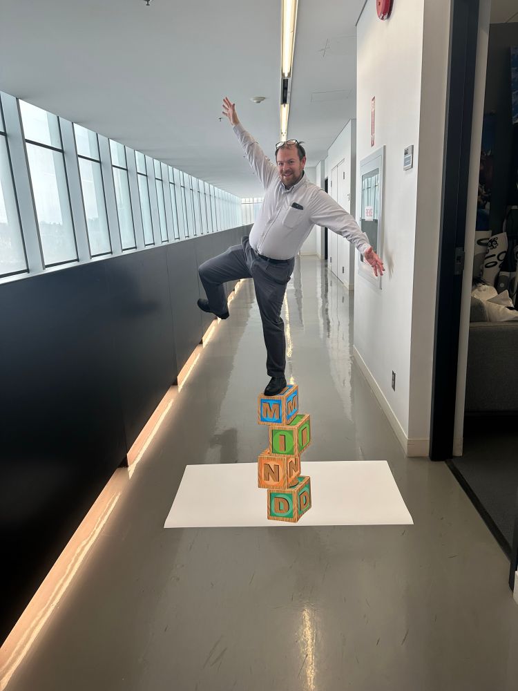 A man standing on a forced perspective image of four blocks reading “mind” in a hallway