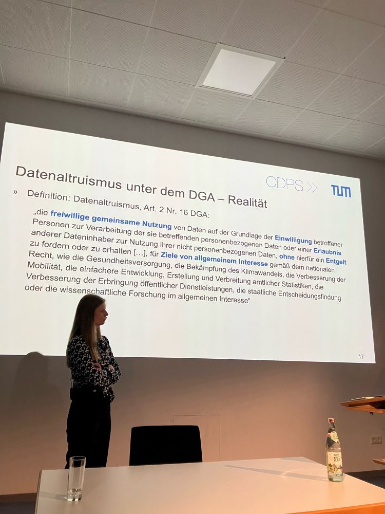 Referentin vor der Präsentation mit folgendem Text: 

Datenaltruismus unter dem DGA - Realität
TLT
» Definition: Datenaltruismus, Art. 2 Nr. 16 DGA:
die freiwillige gemeinsame Nutzung von Daten auf der Grundlage der Einwilligung betroffener Personen zur Verarbeitung der sie betreffenden personenbezogenen Daten oder einer Erlaubnis anderer Dateninhaber zur Nutzung ihrer nicht personenbezogenen Daten, ohne hierfür ein Entgelt
zu fordern oder zu erhaiten [...]. fur Ziele von allgemeinem Interesse gemai dem nationaien
Recht, wie die Gesundheitsversorgung, die Bekämpfung des Klimawandels, die Verbesserung der Mobilität, die einfachere Entwicklung, Erstellung und Verbreitung amtlicher Statistiken, dio Verbesserung der Erbringung Öffentlicher Dienstleistungen, die staatliche Entscheidungsfindung oder die wissenschaftliche Forschung im allgemeinen Interesse*
