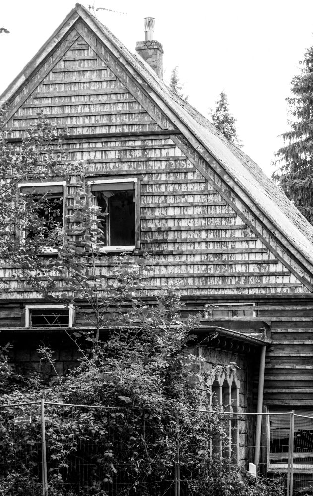 Schwarz-Weiss Aufnahme eines  Hausgiebels, davor ein Bauzaun 