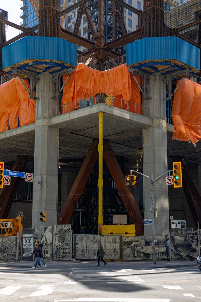 2021-04-08 Toronto Canada - Color Photo taken at the intersection of Bloor and Yonge Street looking south west at the under construction lobby of 1 Bloor West. A large yellow temporary support pillar is flanked by to massive rusting beams in the cavernous lobby. Orange tarps and blue concrete support forms line the top of the image.

Canon R 50mm f2.8 1/640sec iso100