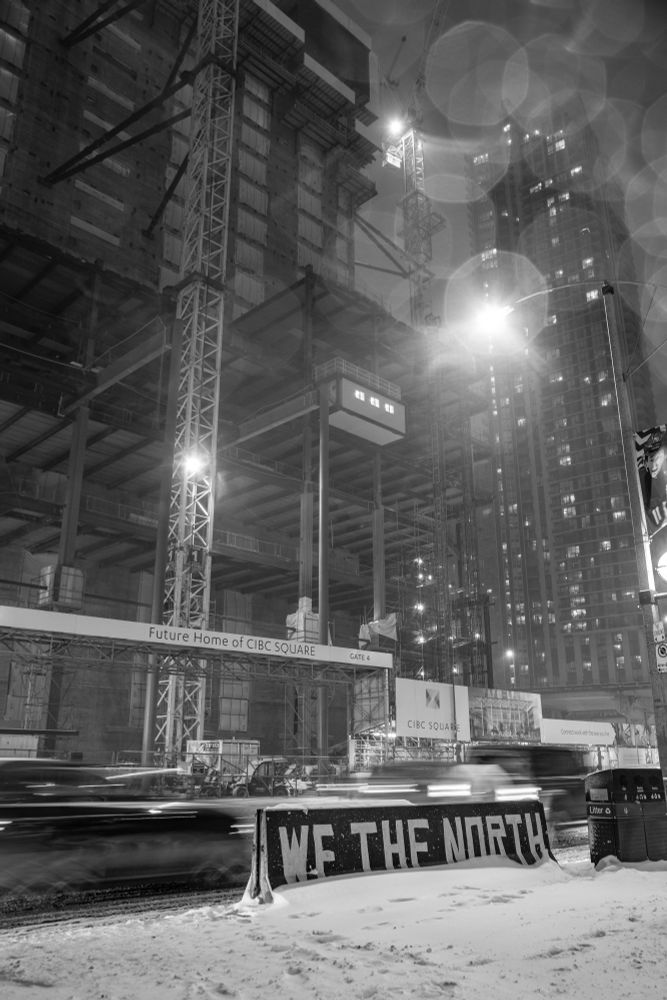 2019-01-29 Toronto, Ontario, Canada - Black and White long exposure photo of a 'We the North' traffic barrier being buried in snow. Behind the barrier traffic appears to be moving quickly while a steel beams structure of the 'future home of CIBC SQUARE' construction are motionless.
Canon 6D 28mm f6.3 1s iso125