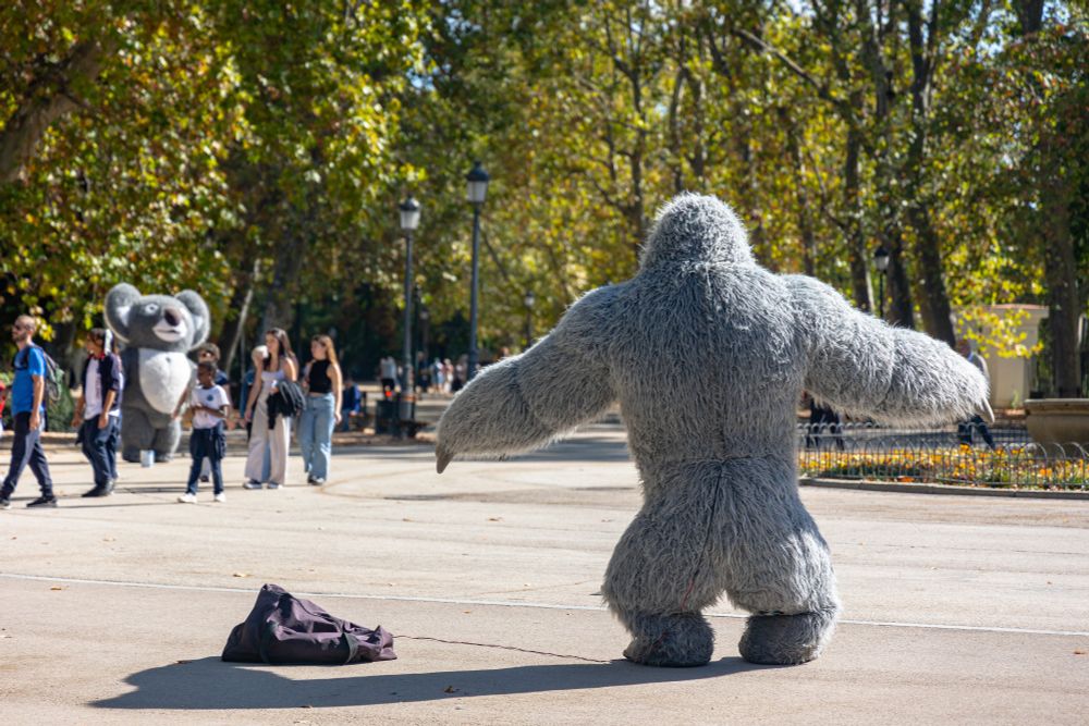 2022-10-13 Madrid Spain - Color photo of a busker in an inflatable gorilla suit with their back to the camera. Unable to lower his arms due to air pressure, it appears he is challenging another inflated Koala busker in a territorial display. Kids walk casual between the buskers uninterested in engaging or recognizing the territorial conflict.

Canon R6 105mm f4.5 1/800sec iso160