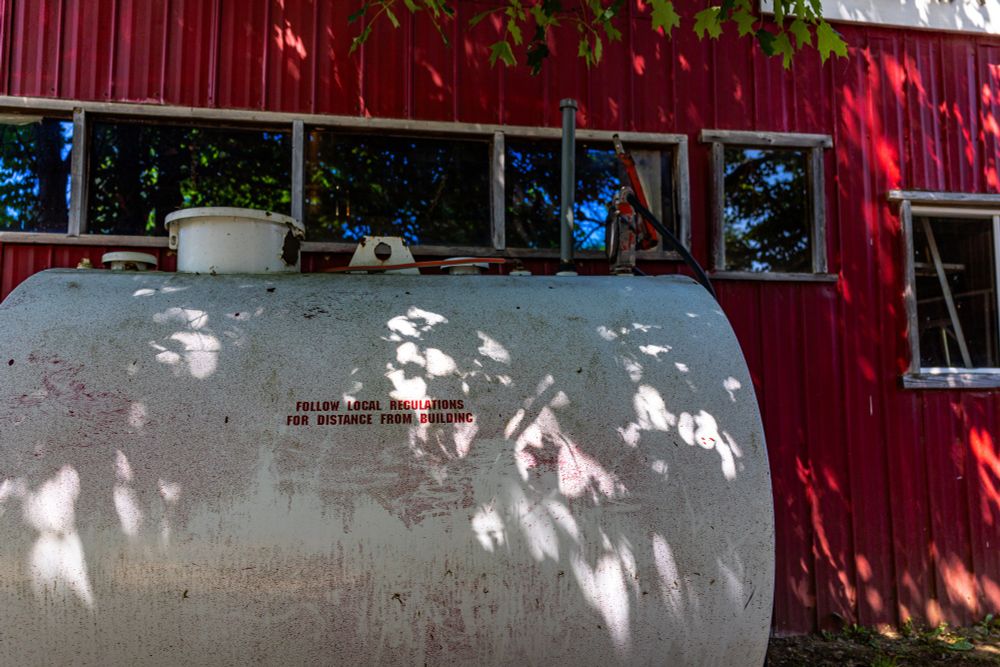 2025-06-29 Ontario: Large white diesel fuel tank nestled next to red metal building with small red text reading;
"follow local regulations
for distance from building"

Canon R6 28mm f3.5 1/250sec iso 160