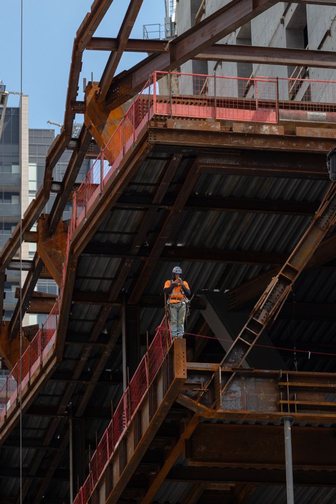 2023-08-09 Toronto, Canada - Colour photo looking up at a construction worker balancing at the end of a rusty girder several hundred feet above ground, lighting a cigarette for a smoke break.
Canon R6 100mm f5.6 1/500s iso400