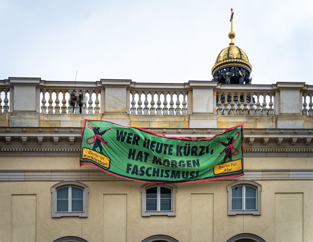Ein grünes Banner wird von der Dachterrasse des Julturforums abgelassen. Auf ihm steht "Wer heute kürzt hat morgen Faschismus"