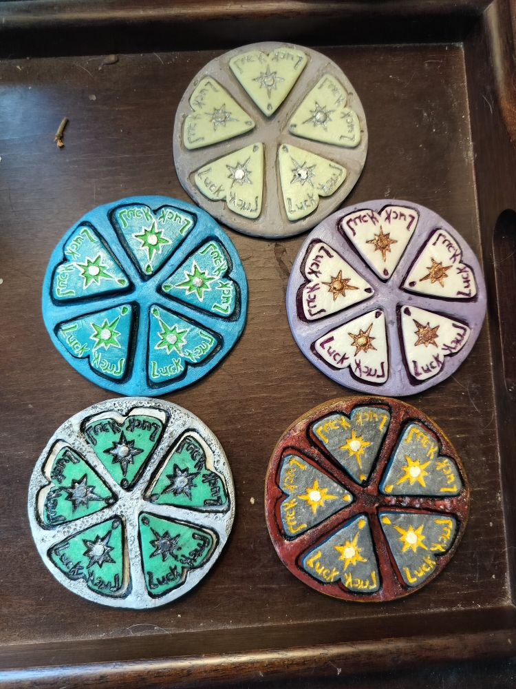 Five colorful resin wheels rest on a tray. Each wheel has five sections, in which sit small chips meant to track the Luck mechanic in ttrpg system Tales of the Valiant.