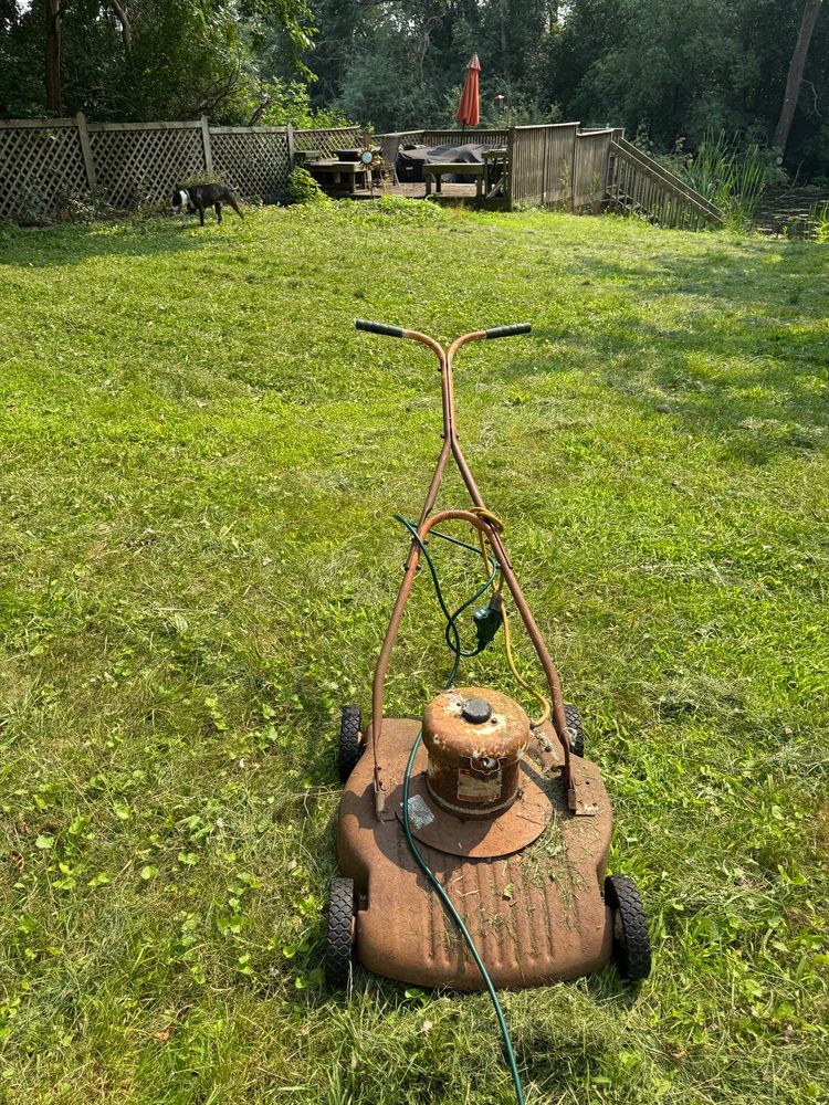 A very old and rusty electric lawnmower with multiple extension cords draped around it.