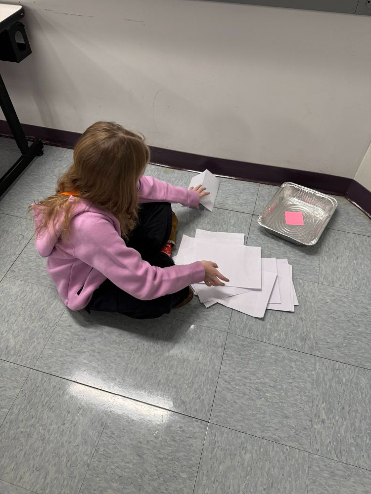Student sitting on the floor and beginning to fold their paper pieces.