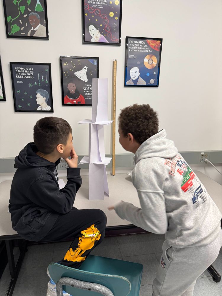Two students discuss how to proceed after building the third tier of their paper tower.