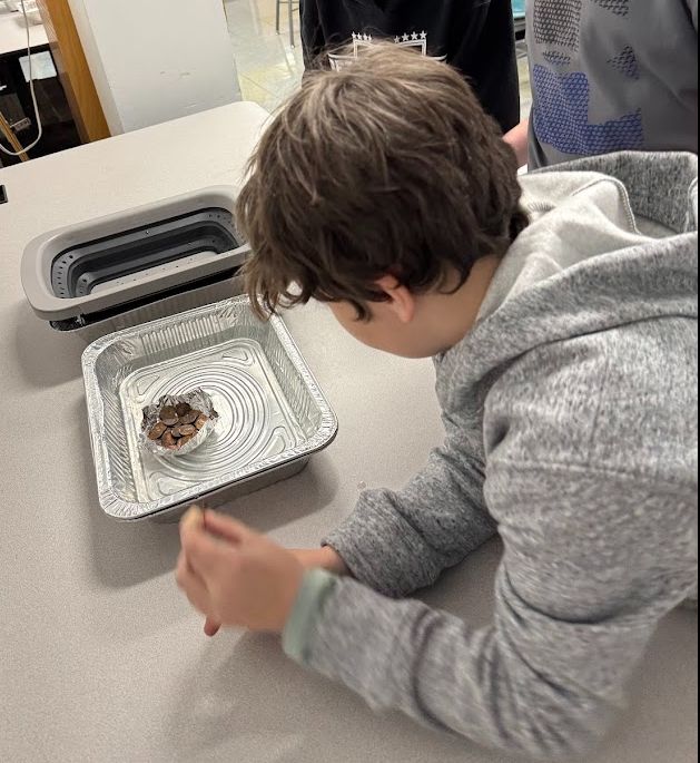 Students adding pennies to their aluminum boat floating in a tray of water.