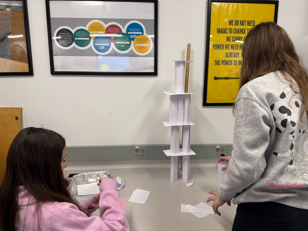Two students work to build their tower out of the paper materials they have constructed.