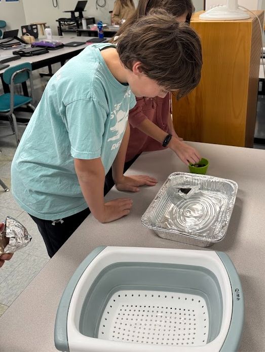 Students adding pennies to their aluminum boat floating in a tray of water.