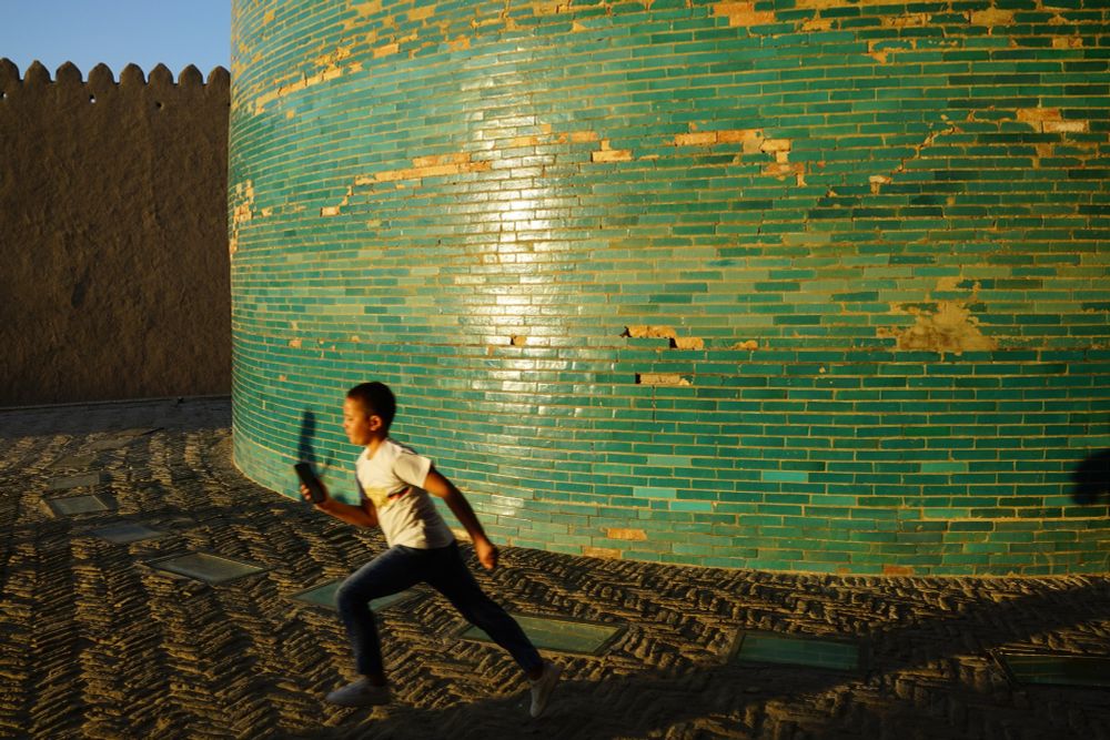 Boy running past greenish-blue tiles of base of Kalta Minor minaret.