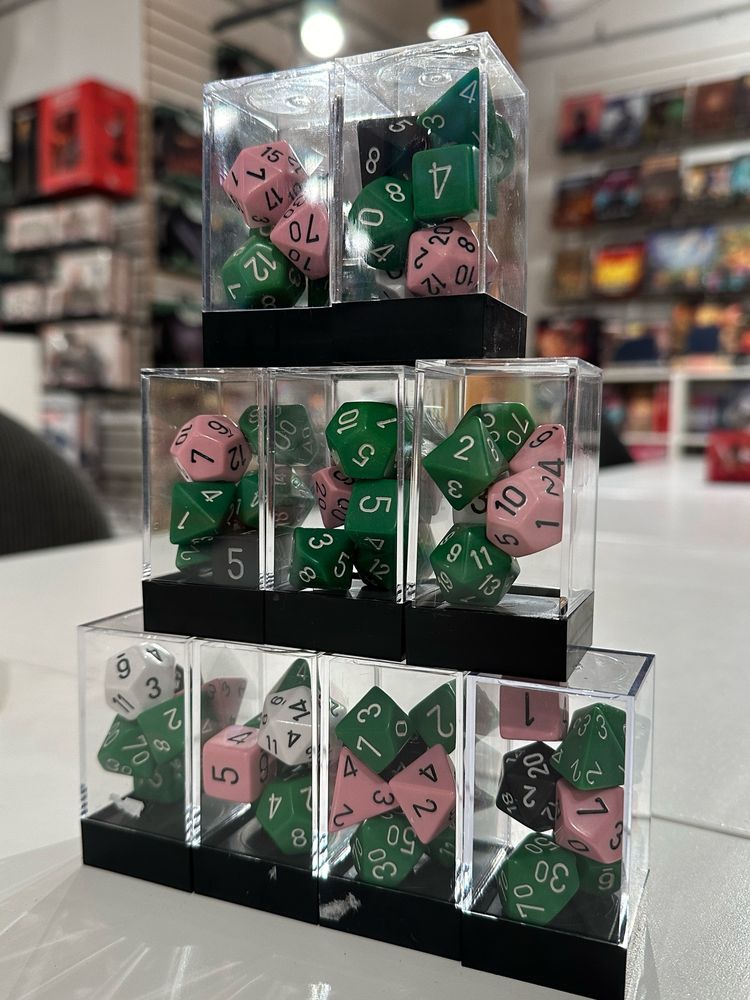 a triangle shaped stack of nine boxes of green, pink, white, and black RPG dice in mixed groups