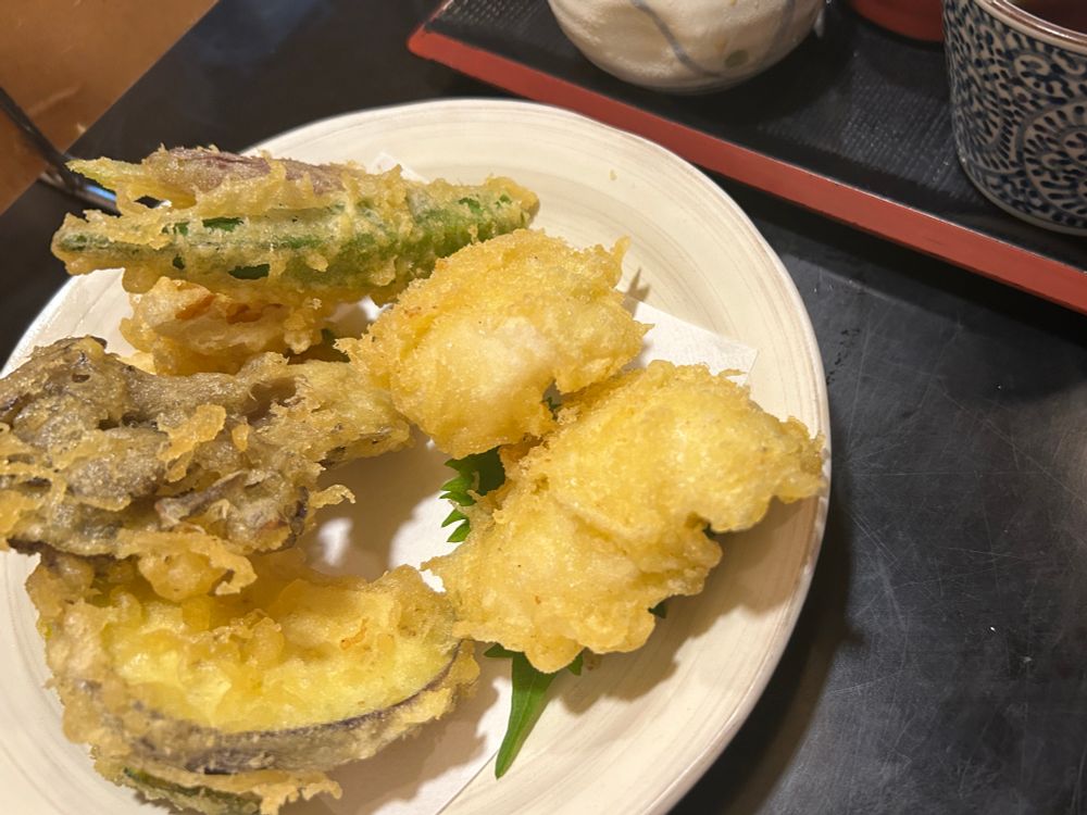 鱧と夏野菜の天ぷらが皿に載っている。画面上側に木製の盆と湯呑みが見切れている