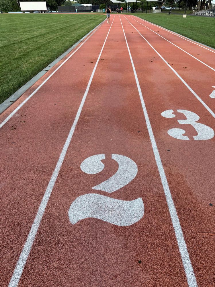 View from a runner in lane two of a track. He’s staring at a straightaway with a couple runners ahead of him.