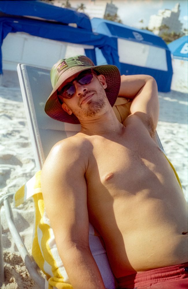 Dylan lounging back on his beach chair with sand and the sky to his back. 