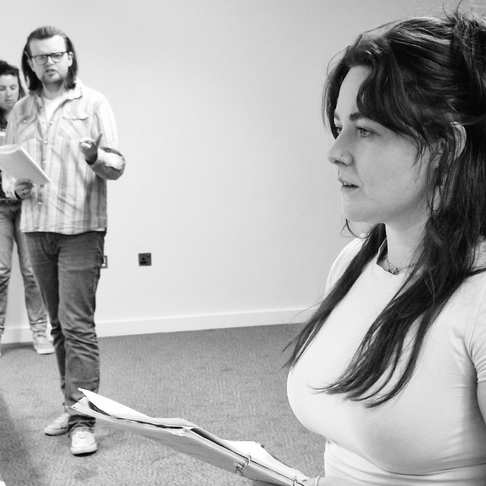 From rehearsals, A close up of an actor in the foreground with two actors further back
