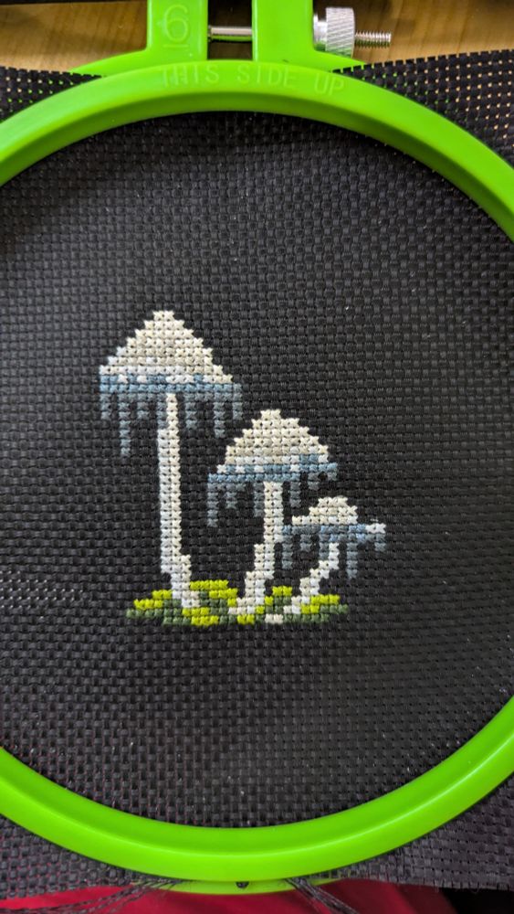 Three ink cap mushrooms cross stitched onto black fabric