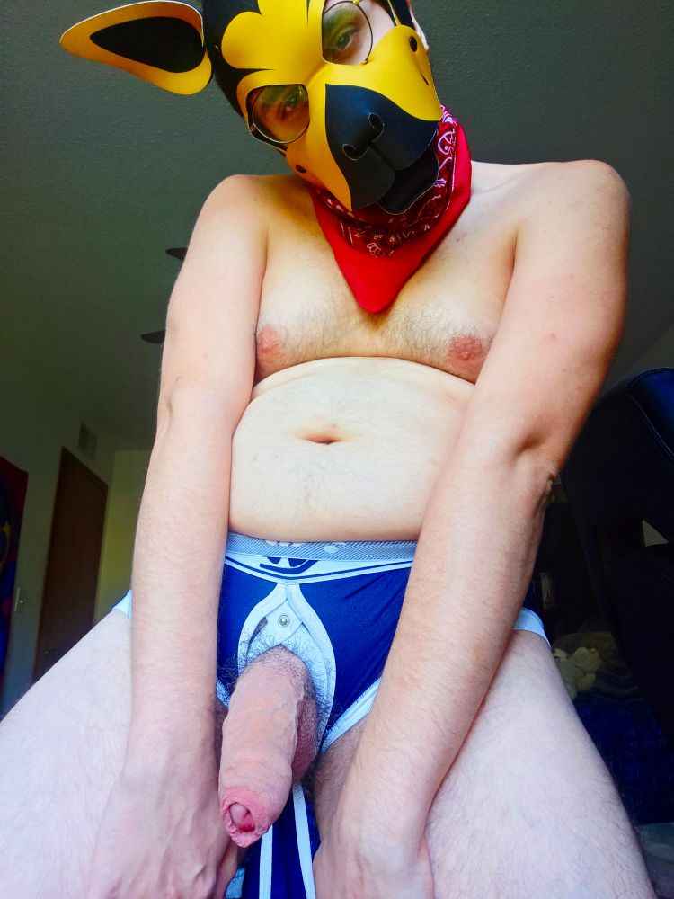 Nawiz standing wearing a red bandana and blue jockstrap, from which his uncut penis is hanging freely for all to see.