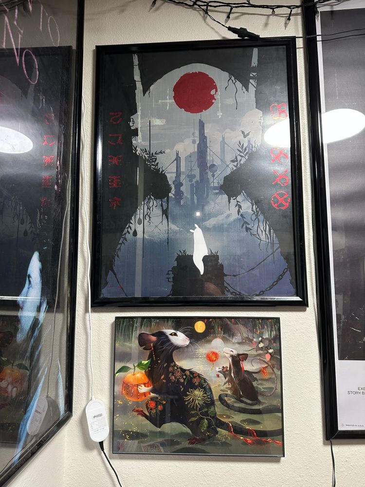 ID: In a wall corner are two visible framed posters, the bottom some black rats carrying cherries, the top a larger artsy Rain World poster. To either side can be seen posters for Pan's Labyrinth and Alien.