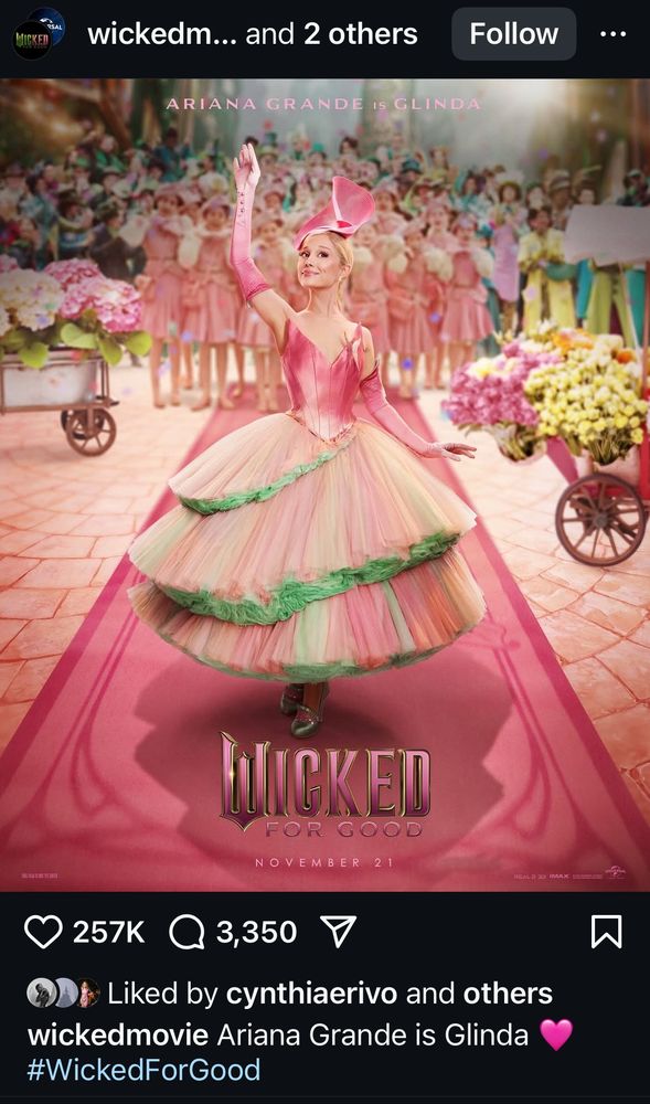 the official wicked: for good character poster for glinda, showcasing her in a pink ballerina- like dress, on a pink carpet, surrounded by the ozians and carts filled with flowers— presumably during the “thank goodness” scene.