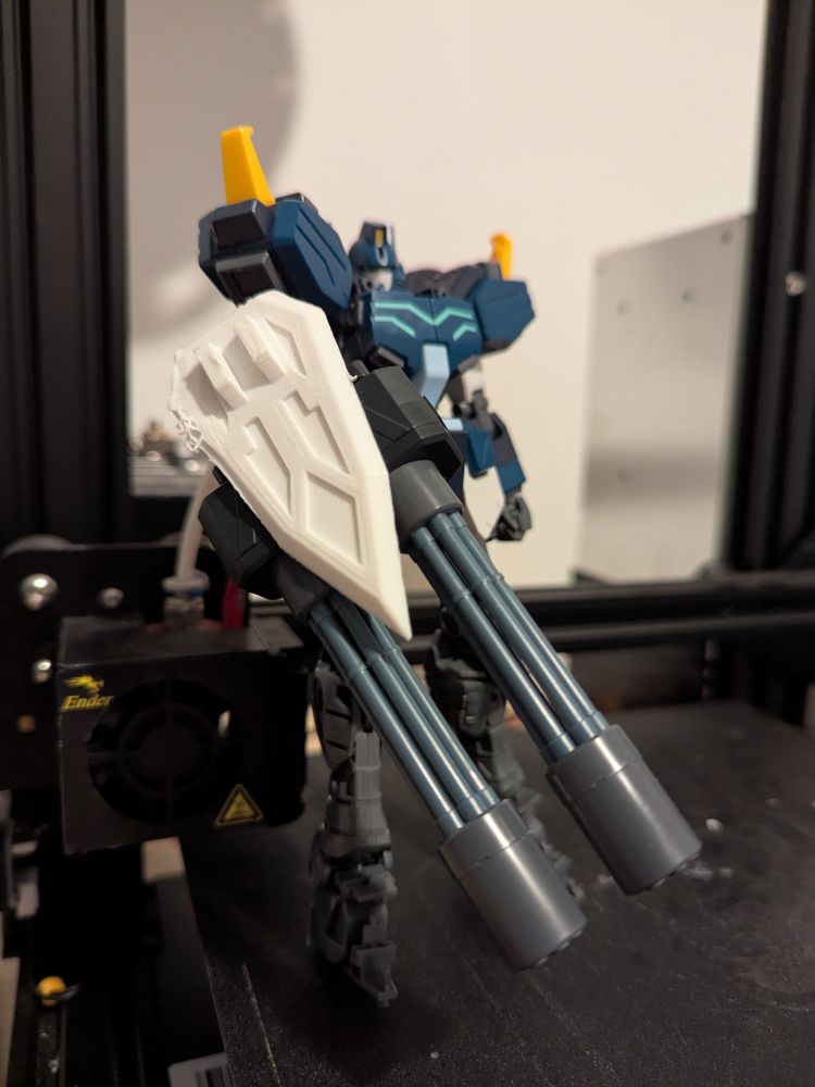 A half assembled Master Grade Heavyarms holding its double Gatling gun with a 3D printed shield attached.