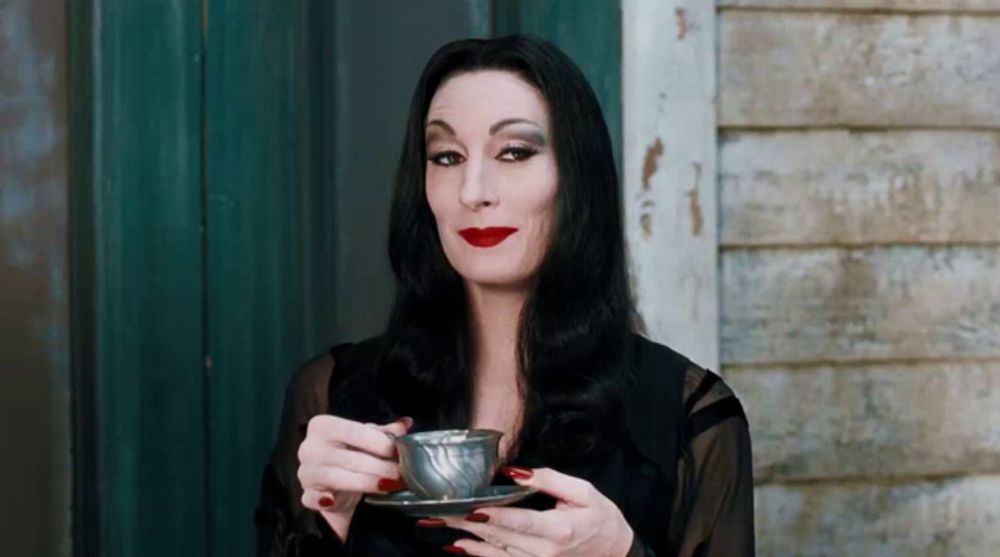 a woman in a black dress is holding a silver cup and saucer