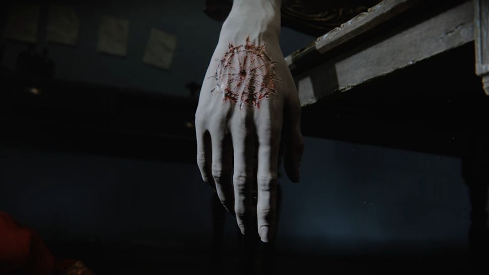 A screenshot from the trailer of the newly announced FromSoftware game, The Duskbloods. In the screenshot, the right hand of a man hangs limply, and there is a bloodied mark etched on the back of it in the shape of a Wheel, with a small hole at the center.