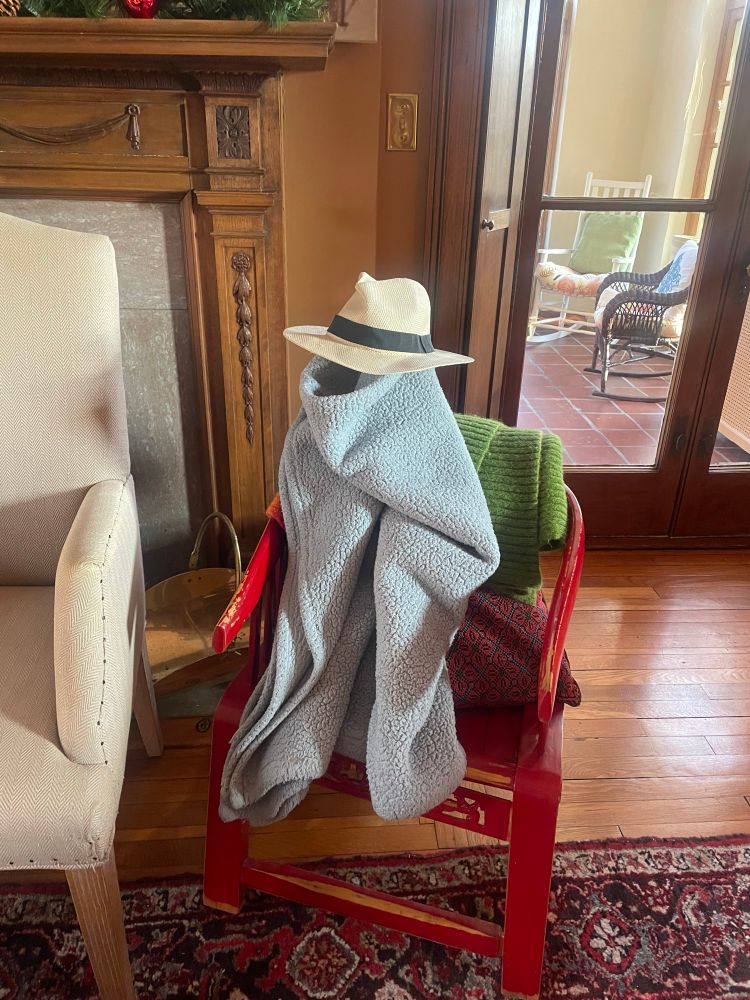 A small humanoid figure made of a light blue blanket with a Panama hat on top. It’s in a living room.