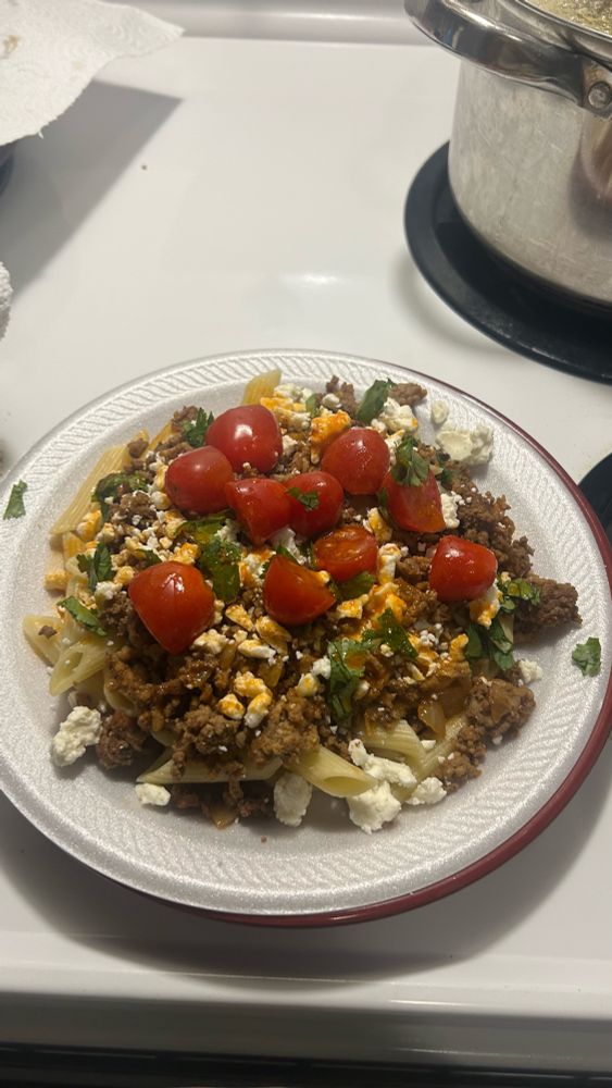 penne pasta topped with ground beef, tzatziki dip, feta cheese, cilantro, halved tomatoes, and paprika butter.