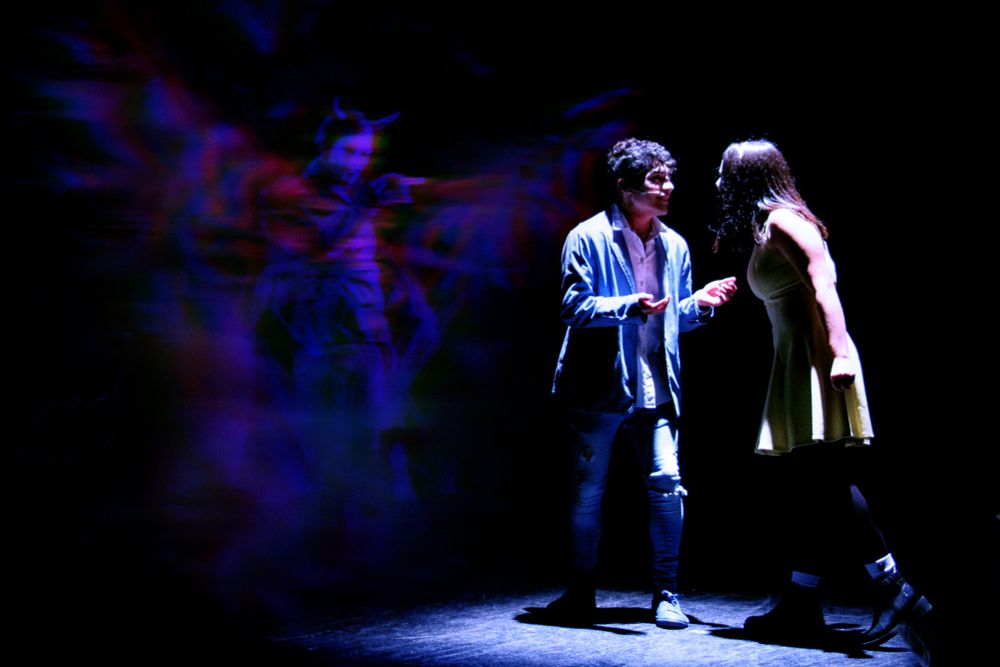 The same picture with a blue filter added. With the reds and greens toned down, the winged creature can now be clearly distinguished as a man with a white face and horned hood. He is pointing at the actress on stage.