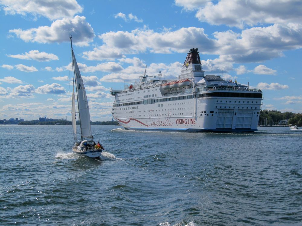 Zwei Schiffe auf dem Weg in den Hafen: links ein Segelboot, rechts ein größeres Fährschiff.