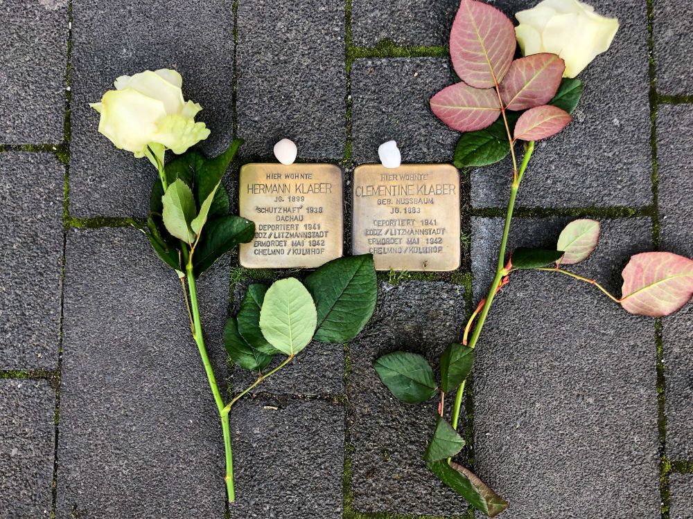 Stolpersteine, verlegt im Bürgersteig für Hermann und Clementine Klaber. Neben den Stolpersteinen liegen weiße Rosen, oberhalb weiße kleine Steine.