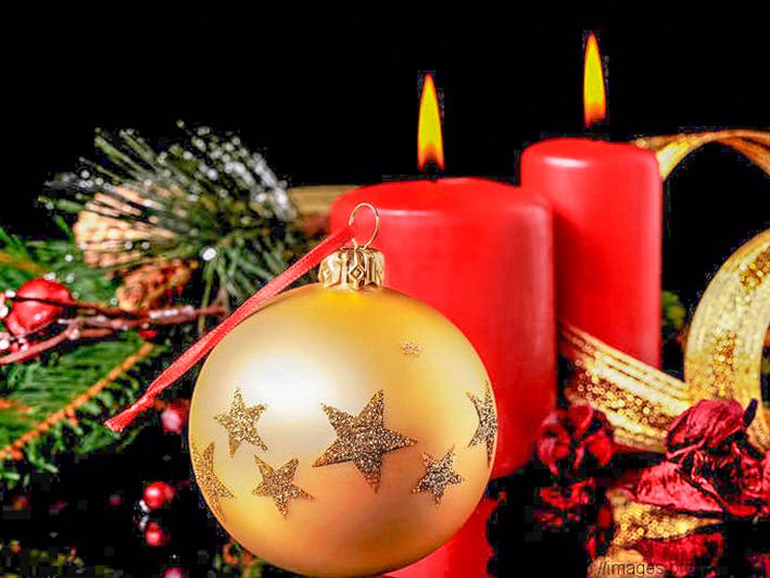 Zwei brennende Kerzen, eine Weihnachtskugel. Tannengrün und weitere Weihnachtsdekoration.