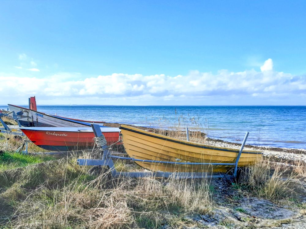 Zwei Boote liegen am Ufer. Zu sehen ist das Meer und ein leicht bewölkter Himmel.