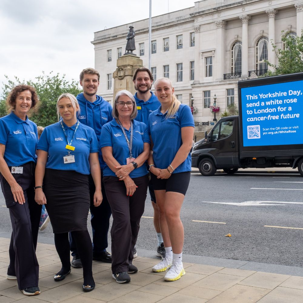 Six members of the Active Together team in Barnsley stand together, with the Yorkshire Cancer Research digivan in the background. 