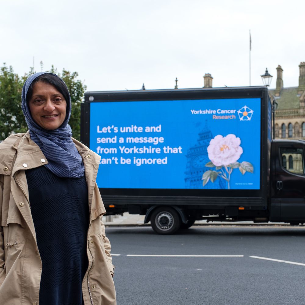 A woman stands in front of the Yorkshire Cancer Research digivan in Bradford. The van displays the words "Let's unite and send a message from Yorkshire that can't be ignored."