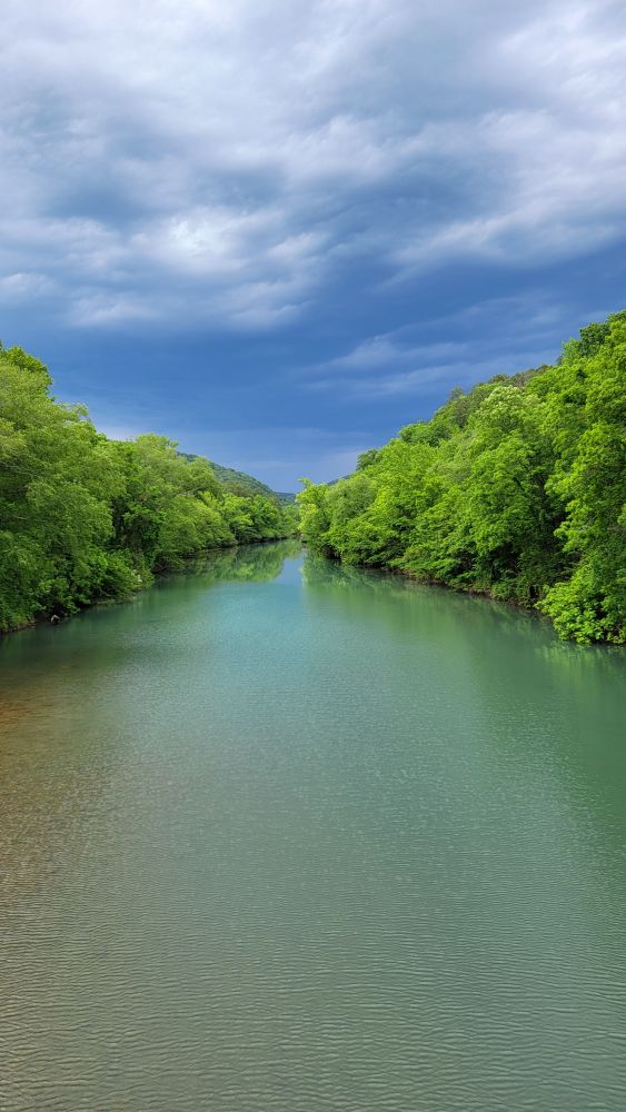 View of tree-lined river with stormy sky