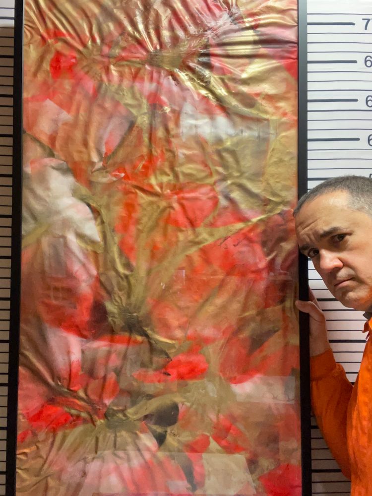 Obra abstracta “Dragontinas: Rubí” en tonos rojos, dorados y negros, fotografiada con luz natural. El artista la sostiene parcialmente visible junto a su rostro, destacando el contraste entre la textura arrugada del vinilo y los colores cálidos que evocan fuego y transformación.