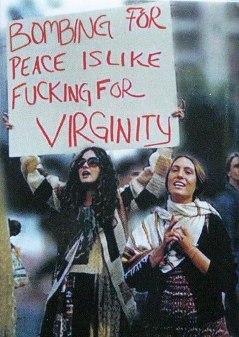 A woman at a protest holding a sign that says, "Bombing for peace is like fucking for virginity". 