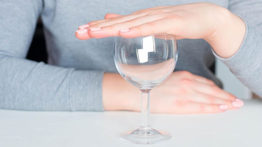 Picture of a white person in a long sleeve gray shirt covering a wine glass with their hand