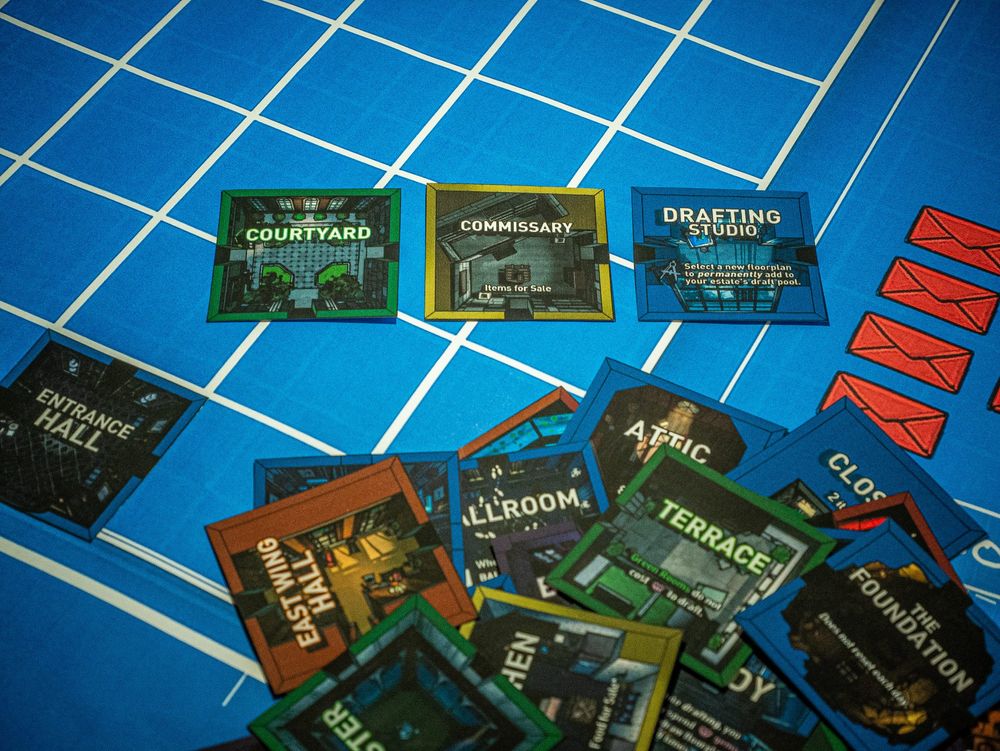 A close-up of a blueprint with a pile of room stickers scattered on top of it, with three room stickers separated for drafting.