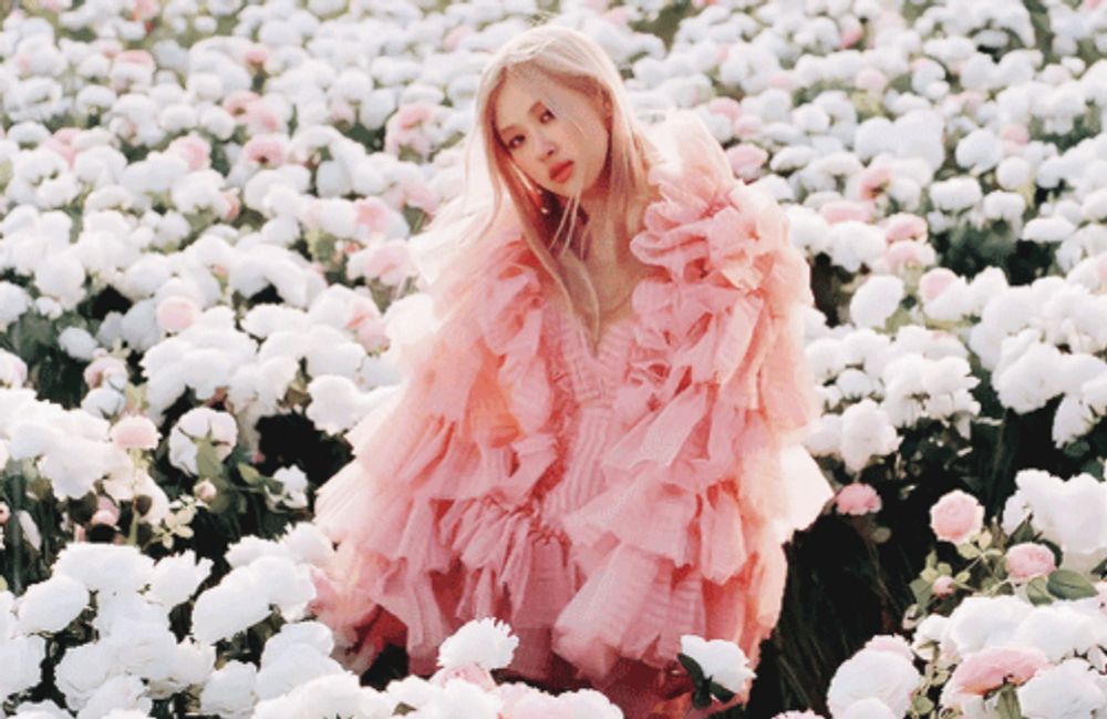 a woman in a pink ruffled dress stands in a field of white flowers