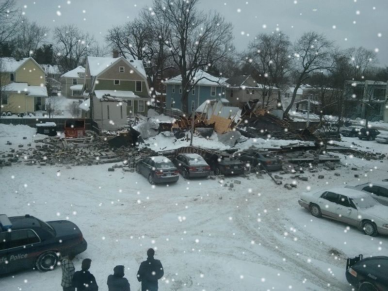 A scene with a building collapsed on several cars. Several people look at the scene. It's covered in snow. Google observed the snow and added a falling snow animation on top of the image.