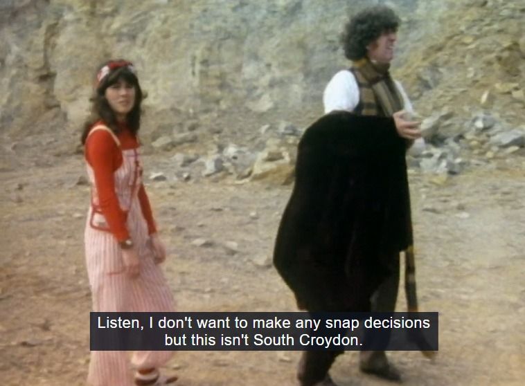Screenshot of a woman in pink overalls and a tall man holding  long coat. They're in a gray rocky environment. The closed caption reads "Listen, I don't want to make any snap decisions but this isn't South Croydon." 