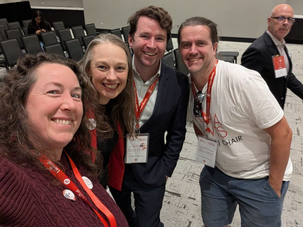 A selfie of 2 men and women wearing red land yards and looking at the camera, and a sidevie w of a man walking by.
