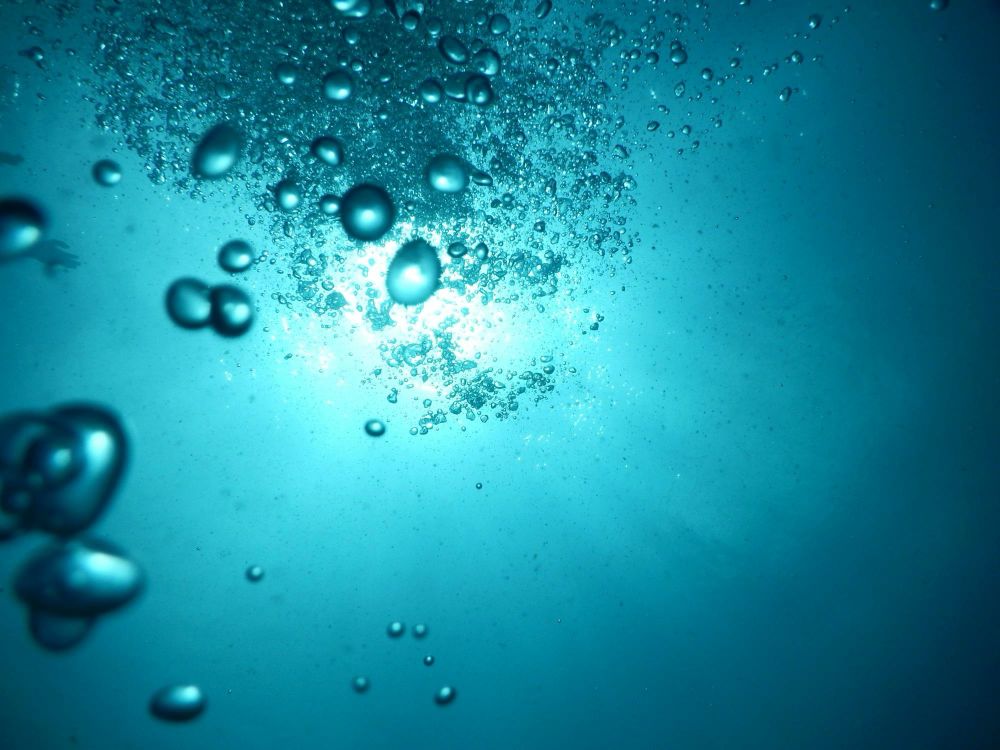 Air bubbles rising toward light in turquoise water 