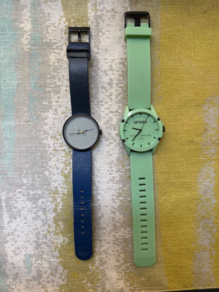 two analog watches, one with a blue leather band and one with a light green silicone band and face