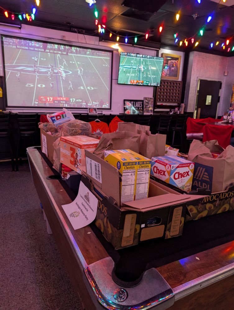 A pool table full of boxes and bags of food in front of a screen playing the Browns/Jets game